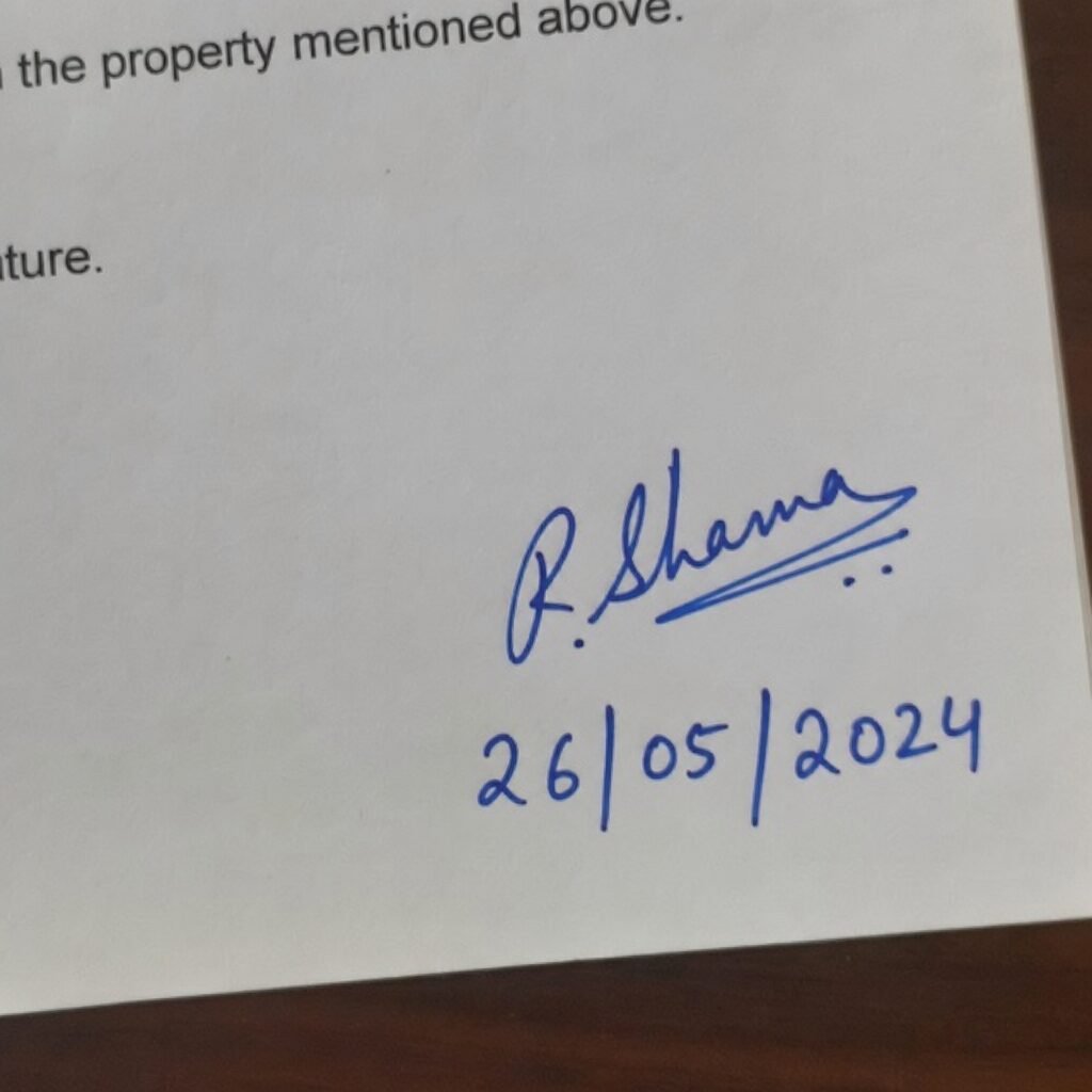 Close up of a signature and the current date written in blue ink on the bottom right corner of a printed paper
